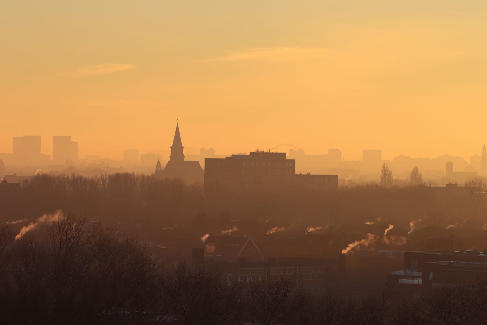 A hazy city skyline at sunset with smoke rising from chimneys